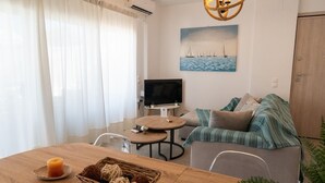 A living room with a TV, sofa, and a painting of sailboats. - Apartment 'Evagelia Luxury  3' with Shared Pool, Wi-Fi and Air Conditioning (?e??ada)