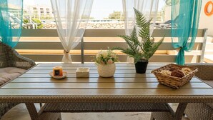 A wicker table with a candle, a vase with flowers, and a basket on a balcony with a view of a building and a pool. - Apartment 'Evagelia Luxury  3' with Shared Pool, Wi-Fi and Air Conditioning (?e??ada)