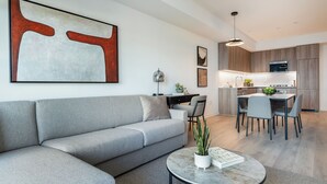 Ein modernes Wohnzimmer mit grauem Sofa, rundem Couchtisch mit Pflanze und einem Essbereich mit Tisch und Stühlen.