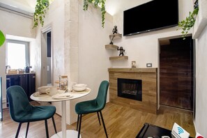 Un salon moderne doté d’une cheminée, d’un téléviseur à écran plat et d’un coin repas comprenant deux chaises et une table mise avec de la vaisselle.