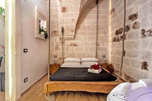 Une pièce rustique avec un lit en bois, une balançoire en corde et un mur en briques.