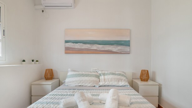 A neatly made bed with towels, a painting of a beach scene, and two bedside tables with decorative vases.