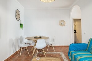 Zona pranzo con un tavolo rotondo, sedie bianche, una sveglia e un divano blu.