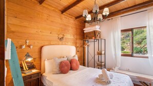 Una habitación de madera con una cama, un banco, un ventanal y una araña.