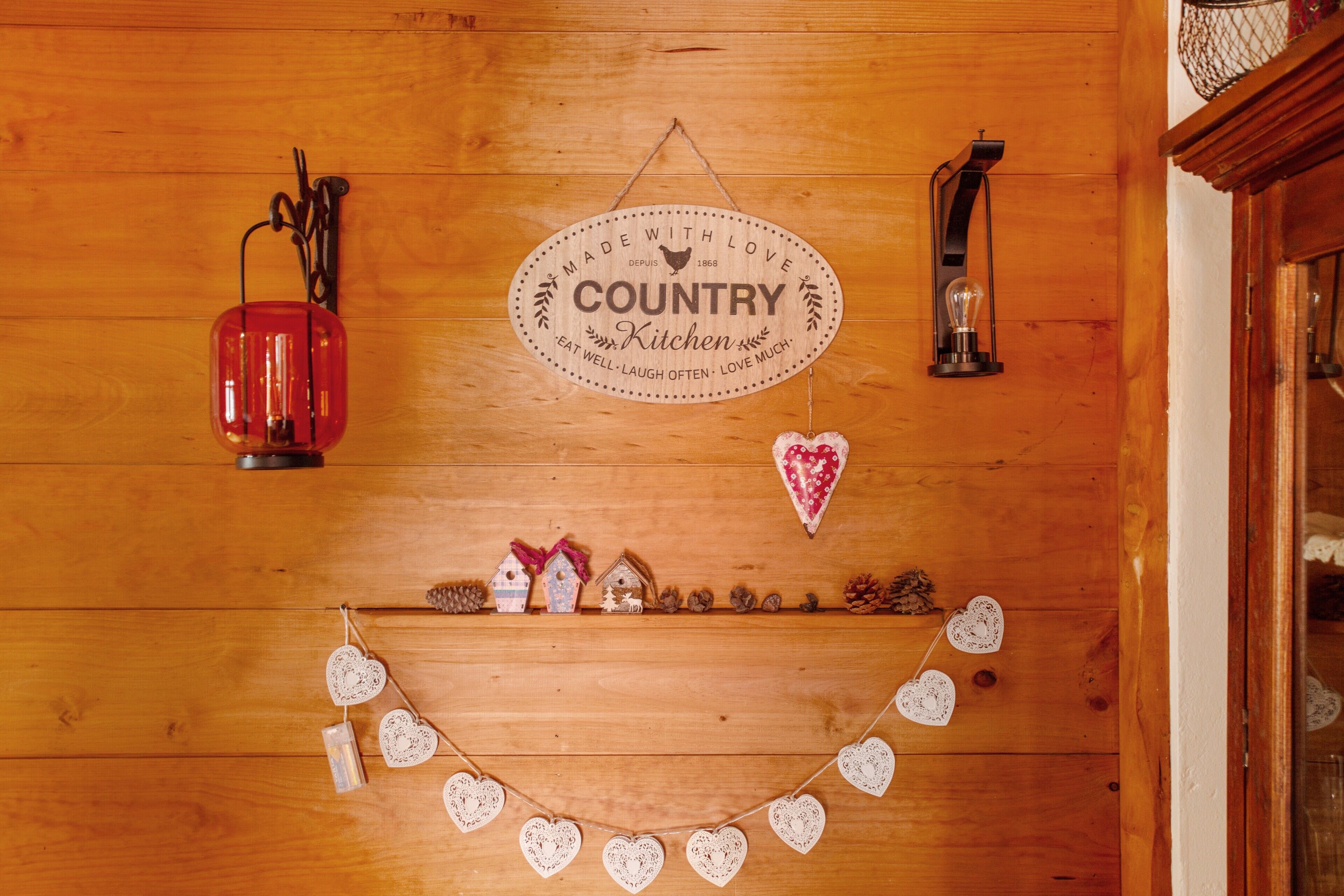 A wooden wall with a sign reading 'COUNTRY Kitchen,' a red lantern, and heart-shaped decorations.