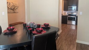 Un coin repas avec une table noire dressée pour six personnes, des bols et des tasses rouges, et un tableau accroché au mur.