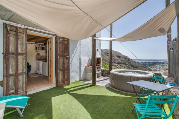 An outdoor patio with a hot tub, a table, and chairs, and a view of the landscape.