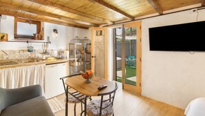 A kitchen with wooden beams, a dining area with a table and chairs, a TV mounted on the wall, and a sliding glass door leading to an outdoor area.