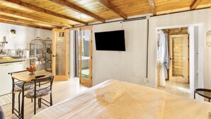 A room with a bed, a television, a wooden ceiling, a door, and a small table with chairs.