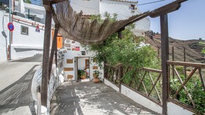A narrow alleyway with a wooden pergola, white buildings with brown accents, and a clear sky.