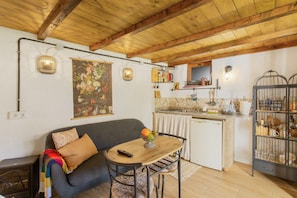 A cozy living room with a sofa, a small table with a fruit bowl, and a kitchen area with a sink and cabinets.