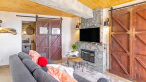 A living room with a gray sofa, a stone fireplace, wooden barn doors, and a mounted TV.