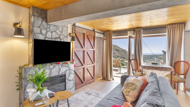 A modern living room with a stone fireplace, a flat-screen TV, a sofa, and a dining area with a table and chairs.