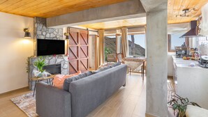A modern living room with a stone fireplace, a flat-screen TV, a grey sofa, and a dining area with a table and chairs.
