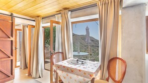 A room with a table set for two, a chair, a wooden door, and a view of a mountain.