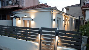 Une maison moderne avec une façade blanche, un toit recouvert de tuiles rouges et une entrée fermée par un portail.
