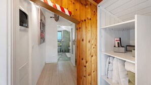 Un couloir avec des lambris en bois, un objet rayé de rouge et de blanc, une porte blanche et une étagère avec des coussins et une télécommande.