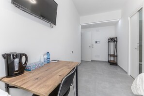 Een moderne kamer met een houten tafel, een waterkoker, flessenwater en een aan de muur bevestigde televisie.
