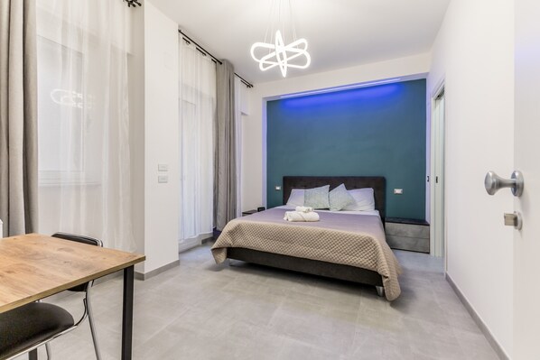 Une chambre d’hôtel moderne avec un lit, une table en bois et un luminaire au plafond original.