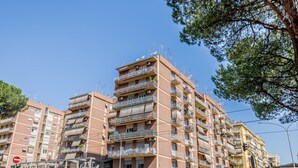 Un immeuble résidentiel à plusieurs étages, doté de balcons, sous un ciel dégagé, et une rue avec des feux de signalisation et un panneau d’interdiction d’accès.