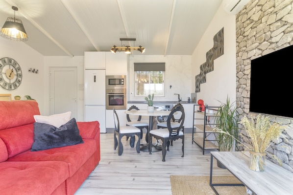 A modern kitchen with a dining area, a red sofa, and a stone wall.