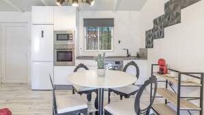 A modern kitchen with white cabinetry, a built-in oven, a microwave, and a dining area with a round table and chairs. - Cottage 'Casita de Ana' with Private Pool, Wi-Fi and Air Conditioning (Conil de la Frontera)