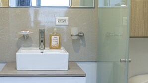 A modern bathroom with a glass shower enclosure, a white sink with a soap dispenser, and wooden cabinets. - Charming Loft Apartment in Cartagena de Indias (Cartagena de Indias)