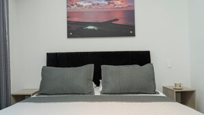 A bed with a headboard, two pillows, a bedside table, and a wall-mounted picture of a sunset over water. - Charming Loft Apartment in Cartagena de Indias (Cartagena de Indias)
