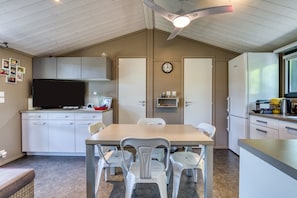 Une cuisine de taille réduite avec des meubles blancs, une table à manger avec des chaises, un ventilateur de plafond et une horloge au mur.