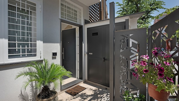 Ein modernes Haus mit grauer Tür, einem Blumentopf und einem Metallzaun.