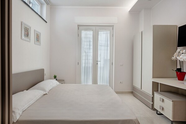 A bedroom with a bed, a nightstand, a dresser, and a window with curtains.