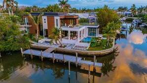 A modern house with a pool, surrounded by water and palm trees. - NEW LUX WATERFRONT HOME- Walk to 5th Ave (Naples)