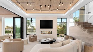 A modern living room with a fireplace, large windows, and a staircase. - NEW LUX WATERFRONT HOME- Walk to 5th Ave (Naples)