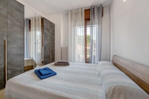 Une chambre d’hôtel avec un grand lit, un miroir, une fenêtre avec des rideaux légers et une vue sur l’extérieur.