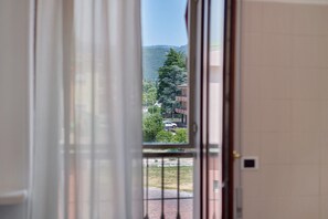 A view through a window with a metal grid, a building with a tiled wall, and a distant mountain.