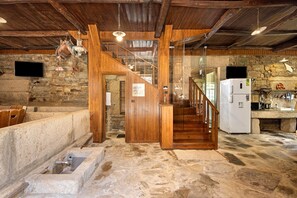 A rustic interior with a stone floor, wooden staircase, stone walls, a wooden door, a white refrigerator, and a mounted television. - Holiday Home 'Casa Do Riacho - Douro' with Mountain View, Private Terrace and Wi-Fi (Armamar)