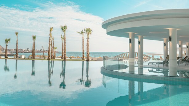 Un espace piscine agrémenté de palmiers et offrant une vue sur la mer.