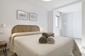 Une chambre à coucher moderne avec un lit, deux tableaux encadrés, une table de chevet et une vue sur un balcon.