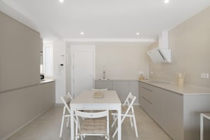 Une cuisine moderne avec des meubles blancs, une table à manger avec des chaises, un four encastré et un four à micro-ondes.