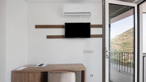 A room with a wooden desk, a mounted flat-screen TV, an air conditioning unit, and a sliding glass door leading to an outdoor balcony. - Property In A Holiday Village 'Quinta Da Pedra Caldeira B' with Mountain View and Air Conditioning (Armamar)