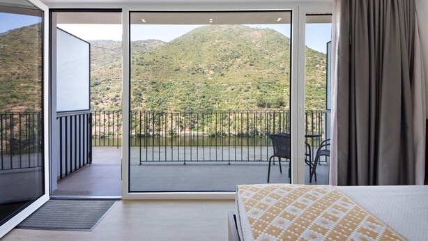 A bedroom with a bed, a balcony with a view of a mountainous landscape, and a dining area with chairs. - Property In A Holiday Village 'Quinta Da Pedra Caldeira B' with Mountain View and Air Conditioning (Armamar)