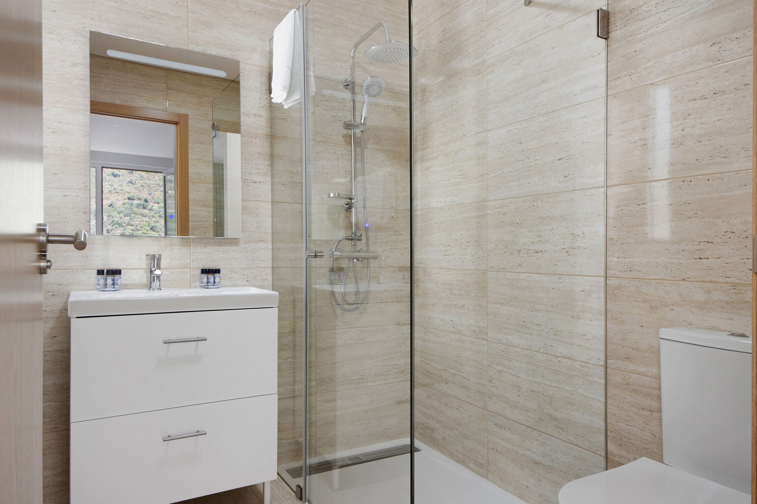 Ein modernes Badezimmer mit einer gläsernen Dusche, einem weißen Waschtisch mit zwei Schubladen und einem großen Spiegel über dem Waschbecken.