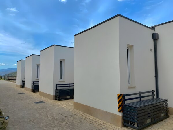 A row of modern, white buildings with flat roofs, windows, and a paved walkway.