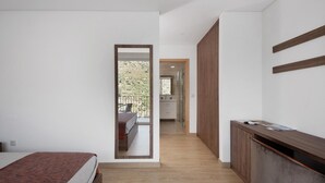 Une chambre avec un lit, un bureau en bois, un miroir et une vue sur un balcon.