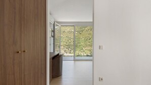 Un couloir avec une armoire en bois, un banc intégré et une grande porte-fenêtre coulissante donnant sur un balcon avec vue sur un paysage vallonné.