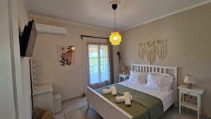 Une chambre à coucher comprenant un lit, des tables de chevet, un luminaire suspendu, un climatiseur fixé au mur et une fenêtre avec des rideaux.
