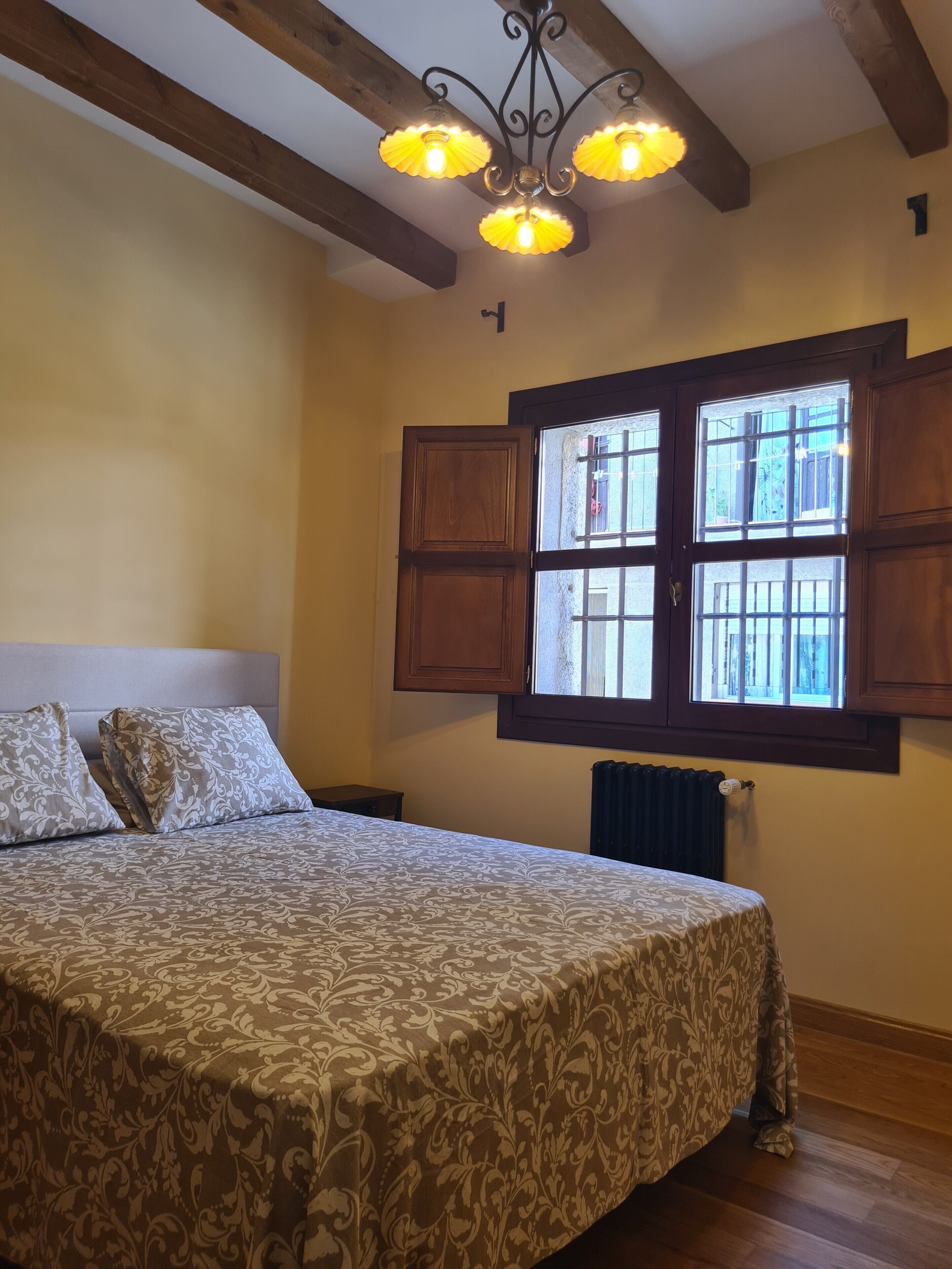A bedroom with a bed, a window with shutters, a radiator, and a chandelier.