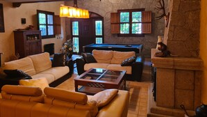 Una sala de estar acogedora con una mesa de billar, sofás de cuero, una mesa de centro de vidrio y una chimenea de piedra.
