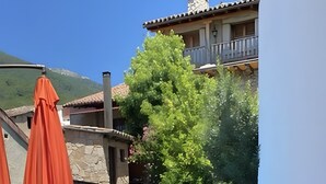 Zona de piscina con mobiliario exterior, un edificio de piedra y una montaña al fondo.