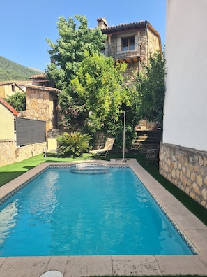 A swimming pool with a stone border, a stone wall, and a tree in the background. - Chalet 'Tu Capricho' with Mountain View, Wi-Fi and Air Conditioning (Piedralaves)